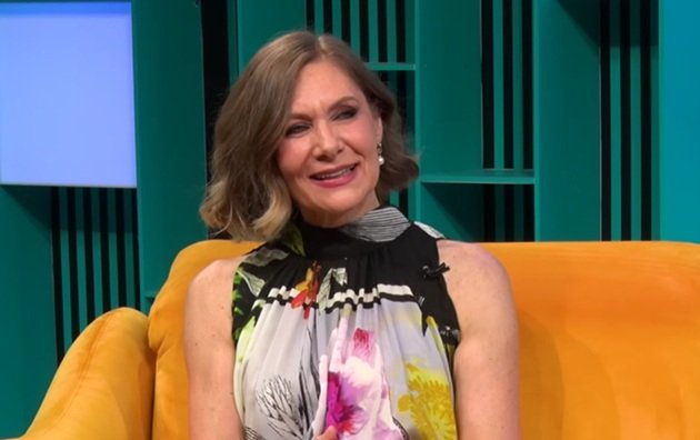 Romanița Iovan z&acirc;mbitoare, &icirc;ntr-o rochie colorată, cu umerii goi, st&acirc;nd pe canapeaua galbenă din platoul emisiunii &bdquo;Online Story by Cornelia Ionescu&rdquo;