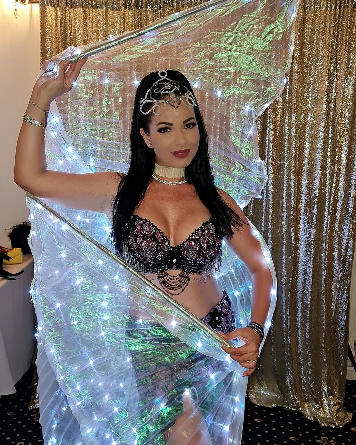Deea Maxer &icirc;n costum de belly dance, pregătită pentru un show, la un eveniment, țin&acirc;nd &icirc;n m&acirc;ini aripile luminoase din componența costumului