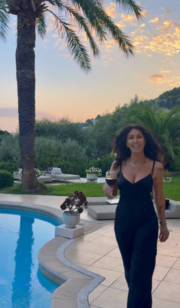 Mihaela Rădulescu la 57 de ani, de ziua ei de naștere, pe marginea piscinei, &icirc;ntr-o rochie neagră, lungă și mulată, țin&acirc;nd &icirc;n m&acirc;nă un pahar de vin