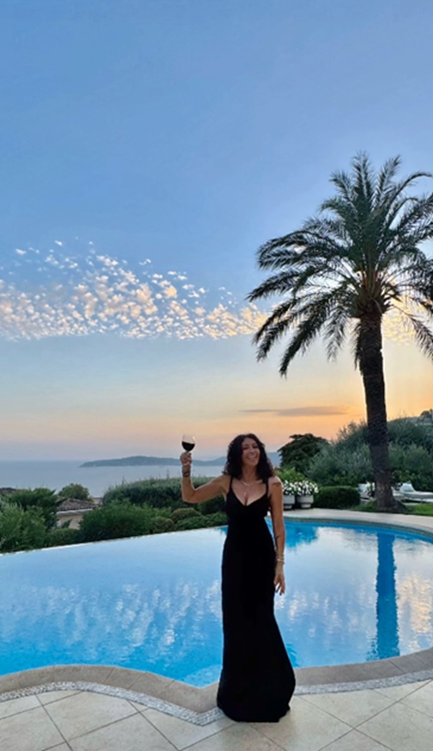 Mihaela Rădulescu &icirc;nchin&acirc;nd un pahar de vin roșu pe marginea piscinei, &icirc;ntr-o rochie lungă care &icirc;i pune silueta &icirc;n valoare