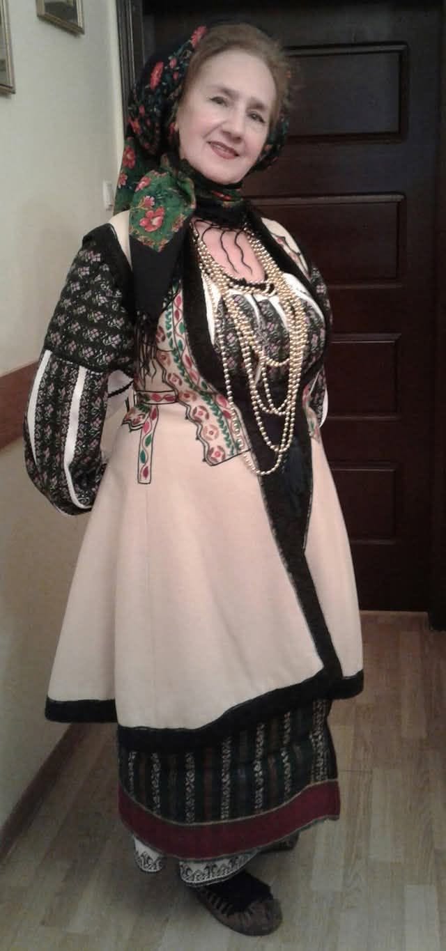 Sofia Vicoveanca z&acirc;mbitoare, &icirc;n costum popular, cu un cojoc alb pe deasupra, cu mărgele la g&acirc;t și batic &icirc;n cap, st&acirc;nd l&acirc;ngă un perete cu m&acirc;inile la spate