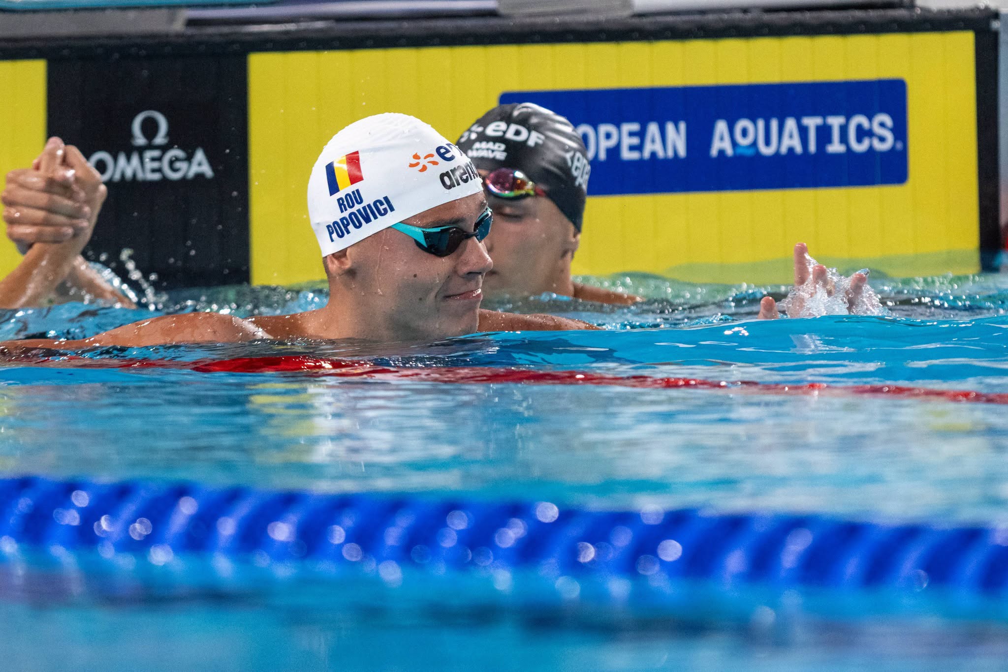 David Popovici la Campionatele Europene de la Paris, d&acirc;nd m&acirc;na cu unul dintre adversarii săi, după ce a luat aurul la 100 m liber