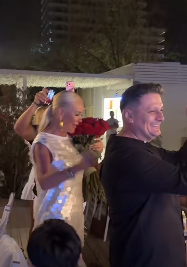 Vica Blochina z&acirc;mbitoare, alături de iubitul ei, &icirc;mbrăcat &icirc;n cămașă neagără, care tocmai i-a oferit un buchet de trandafiri roșii pe care ea &icirc;l ține &icirc;n brațe