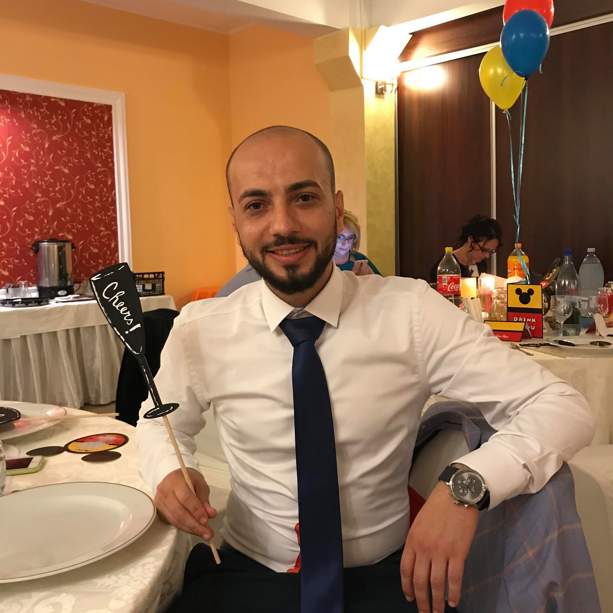 Mircea Marius Totolici, nepotul antrenorului Mircea Rednic, st&acirc;nd la masă, la o petrecere, &icirc;n pantaloni negri, cămașă albă și cu cravată neagră la g&acirc;t
