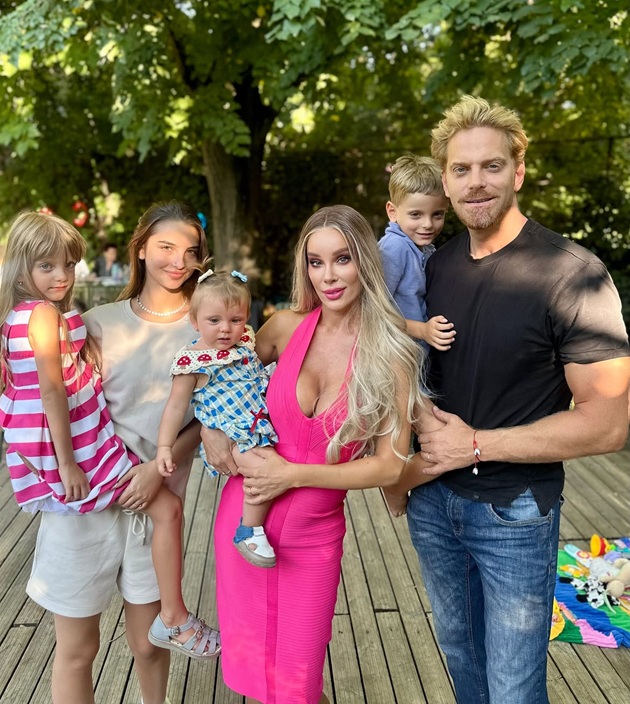 Alina Laufer țin&acirc;nd-o &icirc;n brațe pe Eden, mezina familiei, alături de Ilan Laufer care &icirc;l ține &icirc;n brațe pe&nbsp;Nathaniel&nbsp;și de Karina, fata ei cea mare, care o ține &icirc;n brațe pe Davina, st&acirc;nd toți pe o podea de lemn, &icirc;ntr-un spațiu verde cu mulți copaci