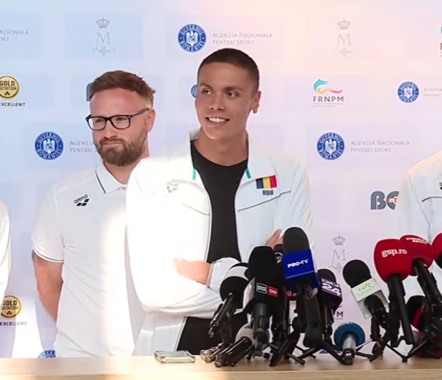 David Popovici vorbind cu presa la &icirc;ntoarcere &icirc;n țară de la Campionatele Europene de la Paris, alături de antrenorul său, Adrian Rădulescu, &icirc;mbrăcați am&acirc;ndoi &icirc;n alb
