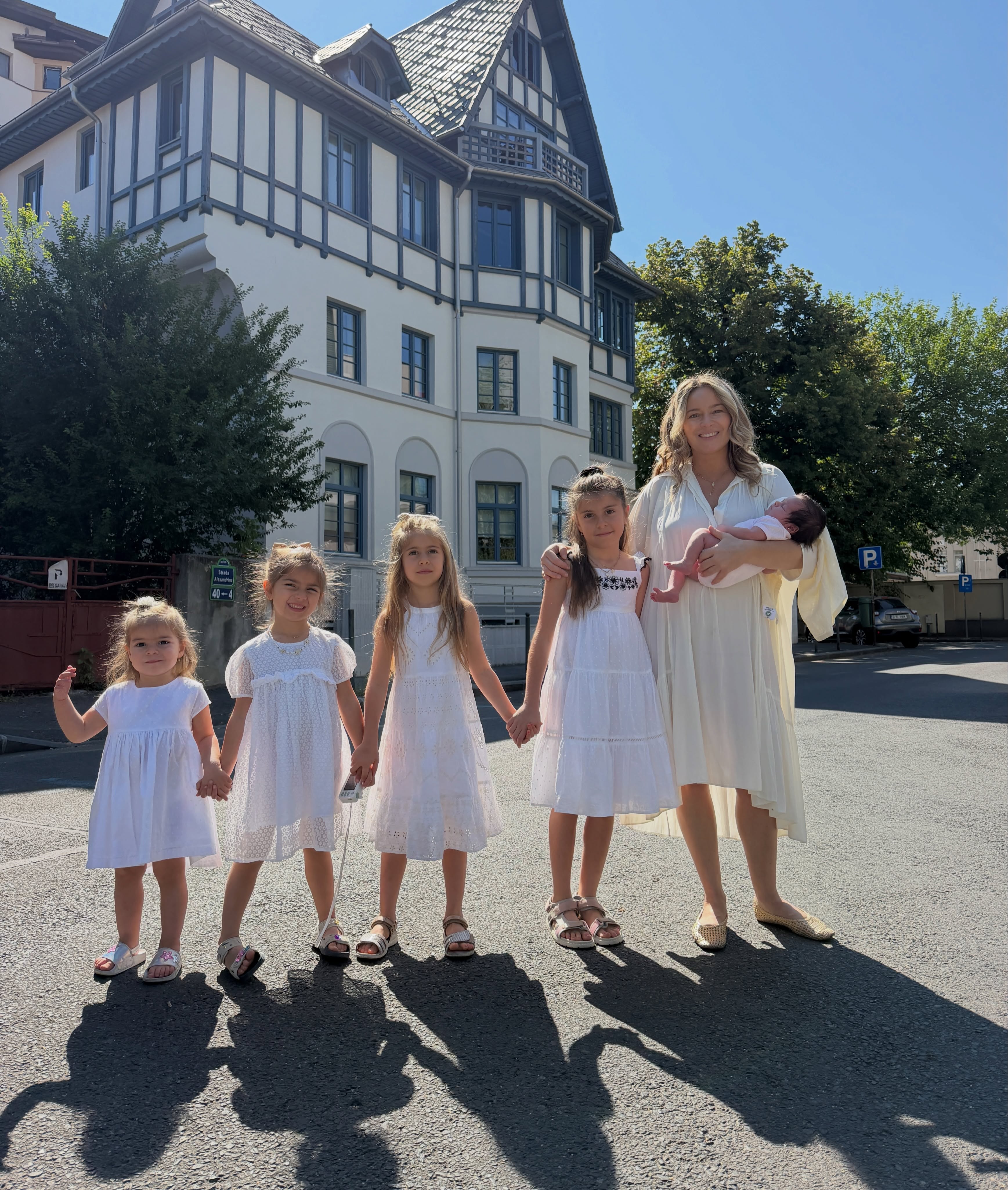 Laura Cosoi alături de cele cinci fetițe ale sale, &icirc;mbrăcate toate &icirc;n alb, &icirc;n timp ce ea o ține &icirc;n brațe pe mezina Nina, iar celelalte se țin de m&acirc;nă l&acirc;ngă ea, 