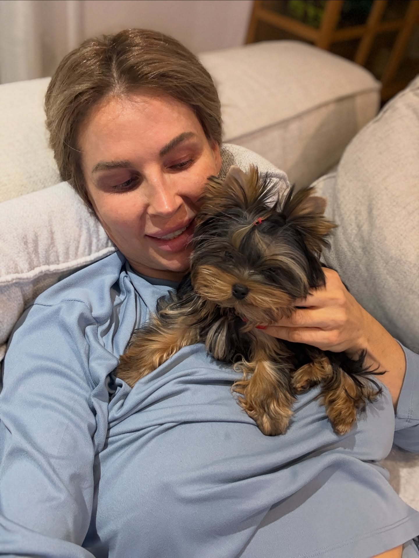 Andreea Bănică st&acirc;nd &icirc;ntinsă pe canapea și țin&acirc;ndu-l pe pieptul ei pe Rutzy, cățelul familiei