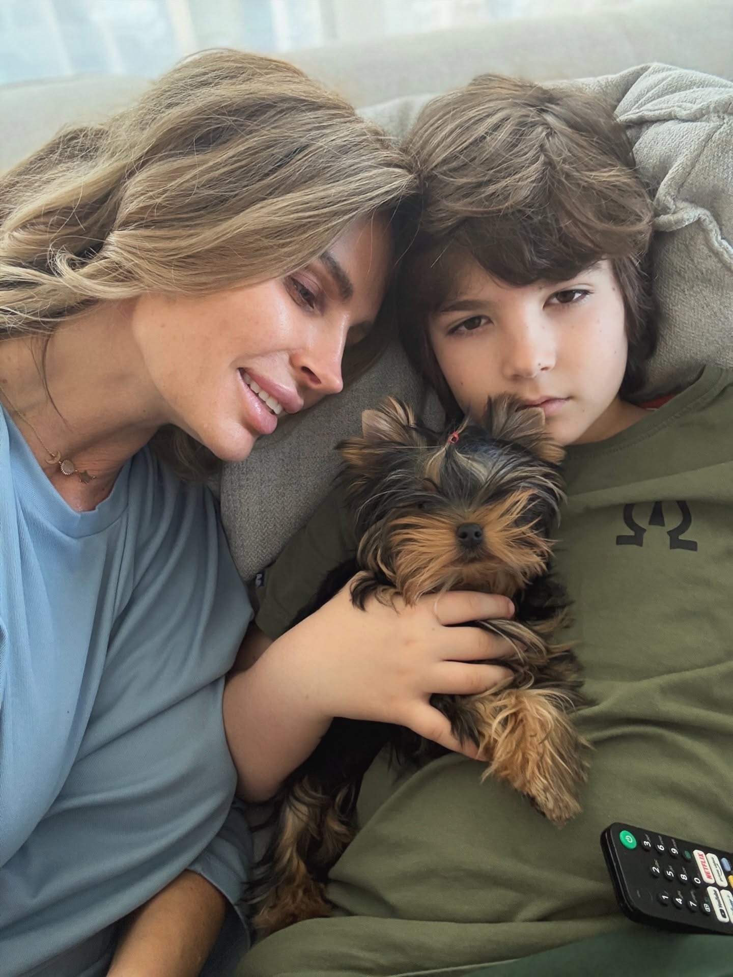 Andreea Bănică st&acirc;nd pe canapea, alături de fiul ei Noah care &icirc;l ține &icirc;n brațe pe Rutzy, animalul lor de companie