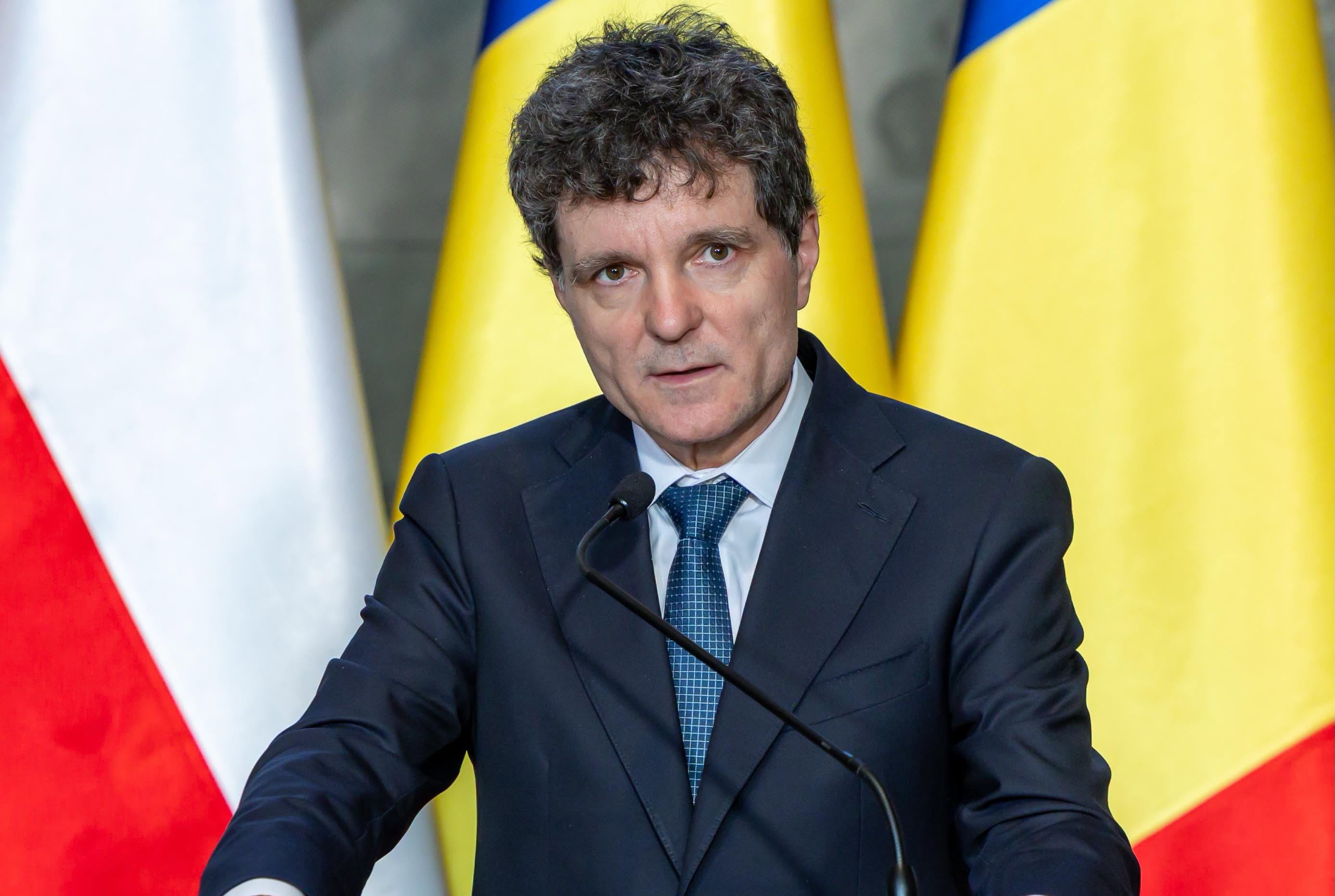 președintele Nicușor Dan vorbind la un pupitru, cu microfonul &icirc;n față și cu mai multe steaguri de mari dimensiuni &icirc;n spate, &icirc;n timp ce era &icirc;mbrăcat &icirc;ntr-un costum bleumarin
