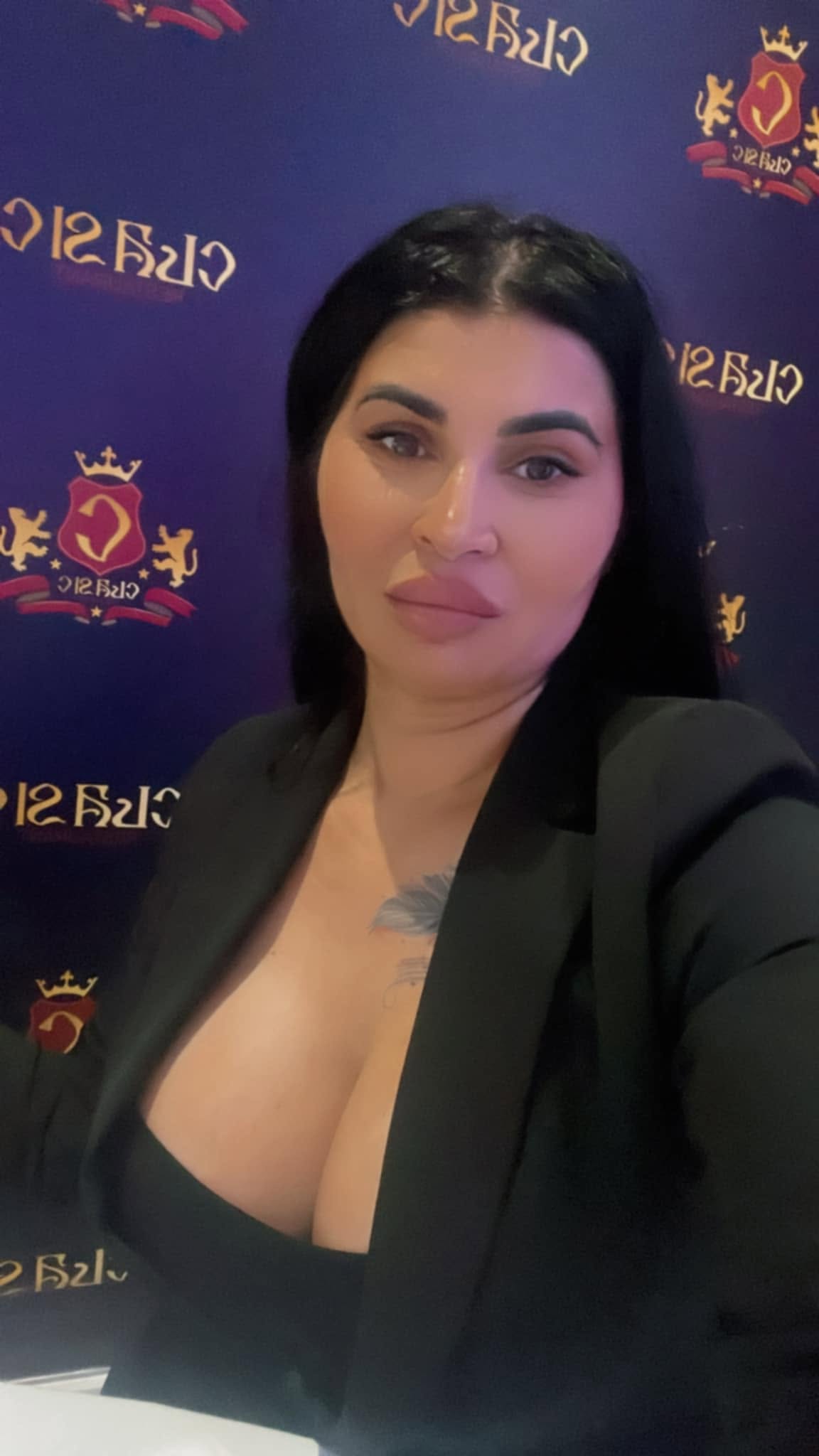 Ramona de la Clejani făc&acirc;ndu-și un selfie, &icirc;mbrăcată &icirc;n tricou negru și sacou negru, cu tatuajul de pe piept la vedere