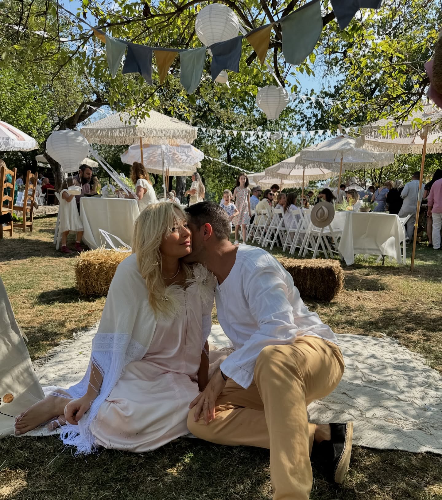 Laura Cosoi și soțul ei la botezul Aidei, penultima lor fiică, &icirc;n timp ce stăteau pe iarbă, pe o pătură albă, iar ea purta o rochie albă și el pantaloni bej și cămașă albă