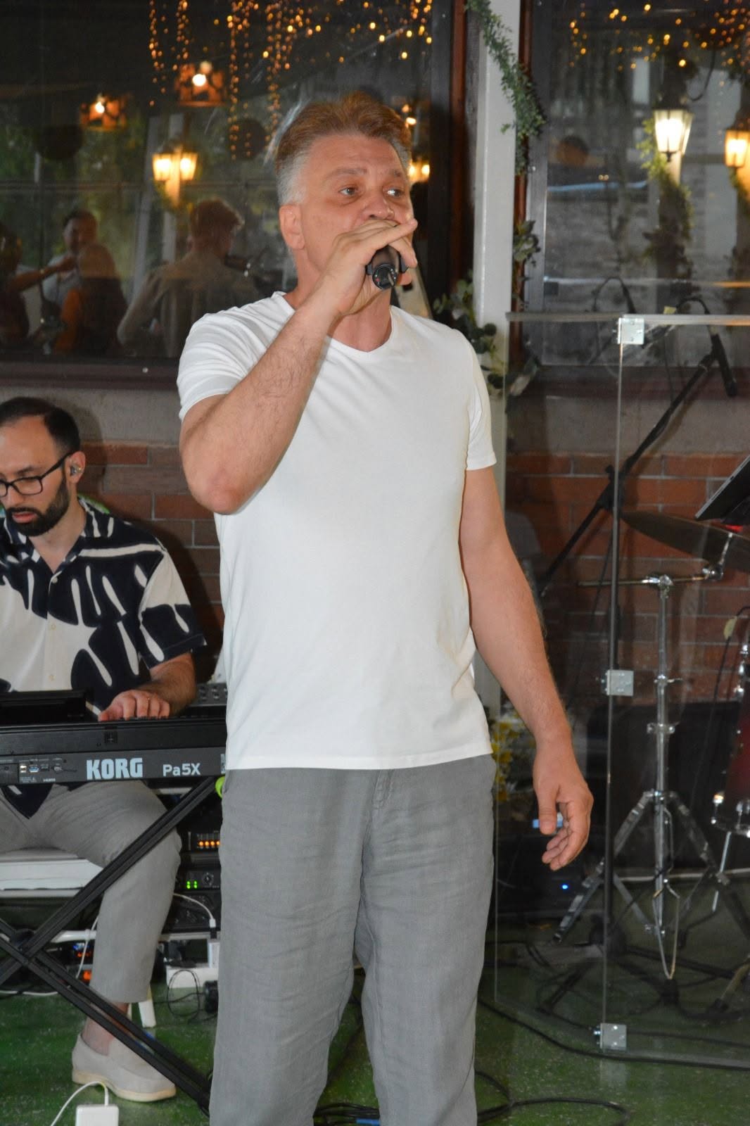 Mihai Onilă &icirc;n tricou alb și pantaloni gri, c&acirc;nt&acirc;nd &icirc;ntr-un restaurant