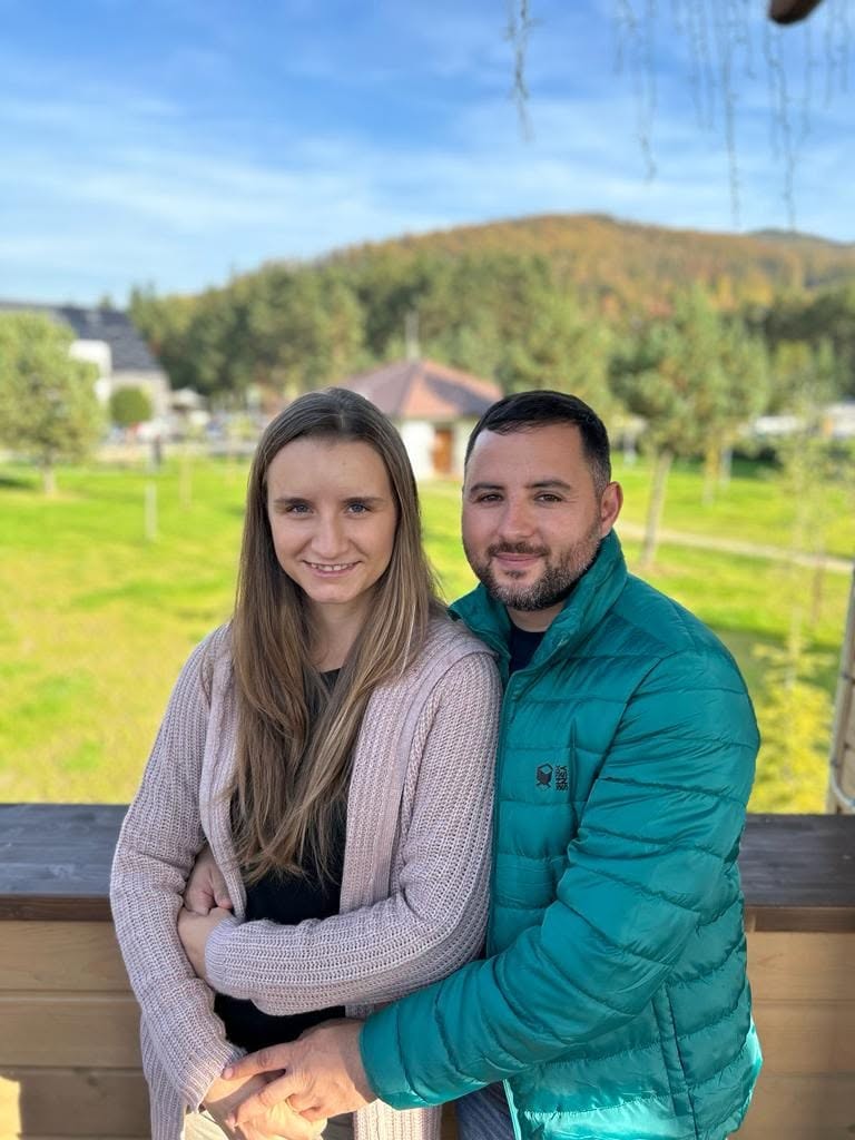 Alexandra Ivanov ținută &icirc;n brațe de soțul ei, Gabriel Ivanov, &icirc;n timp ce erau am&acirc;ndoi &icirc;mbrăcați &icirc;n haine groase, la munte, pe terasa unei case cu priveliște spre munți