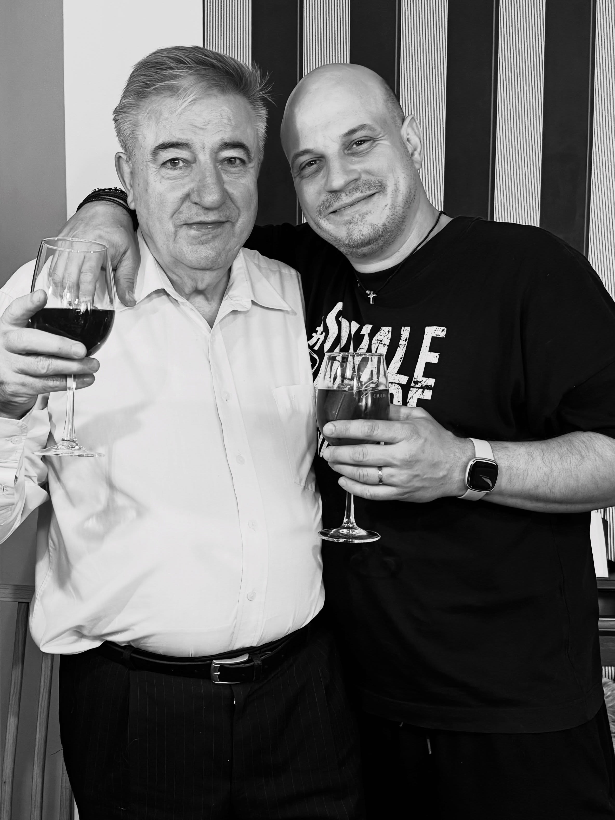 Vlad Huidu alături de tatăl său, Florin Huidu, &icirc;mbrăcați &icirc;n negru și alb, țin&acirc;nd &icirc;n m&acirc;ini două pahare de vin, &icirc;n timp ce fiul &icirc;și ține tatăl de g&acirc;t și z&acirc;mbește l&acirc;ngă el