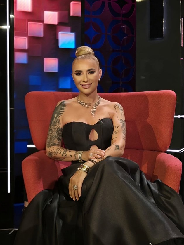 Anamaria Prodan într-o rochie roșie de seară, cu părul prins într-un coc elegant, stând pe un fotoliu roșu