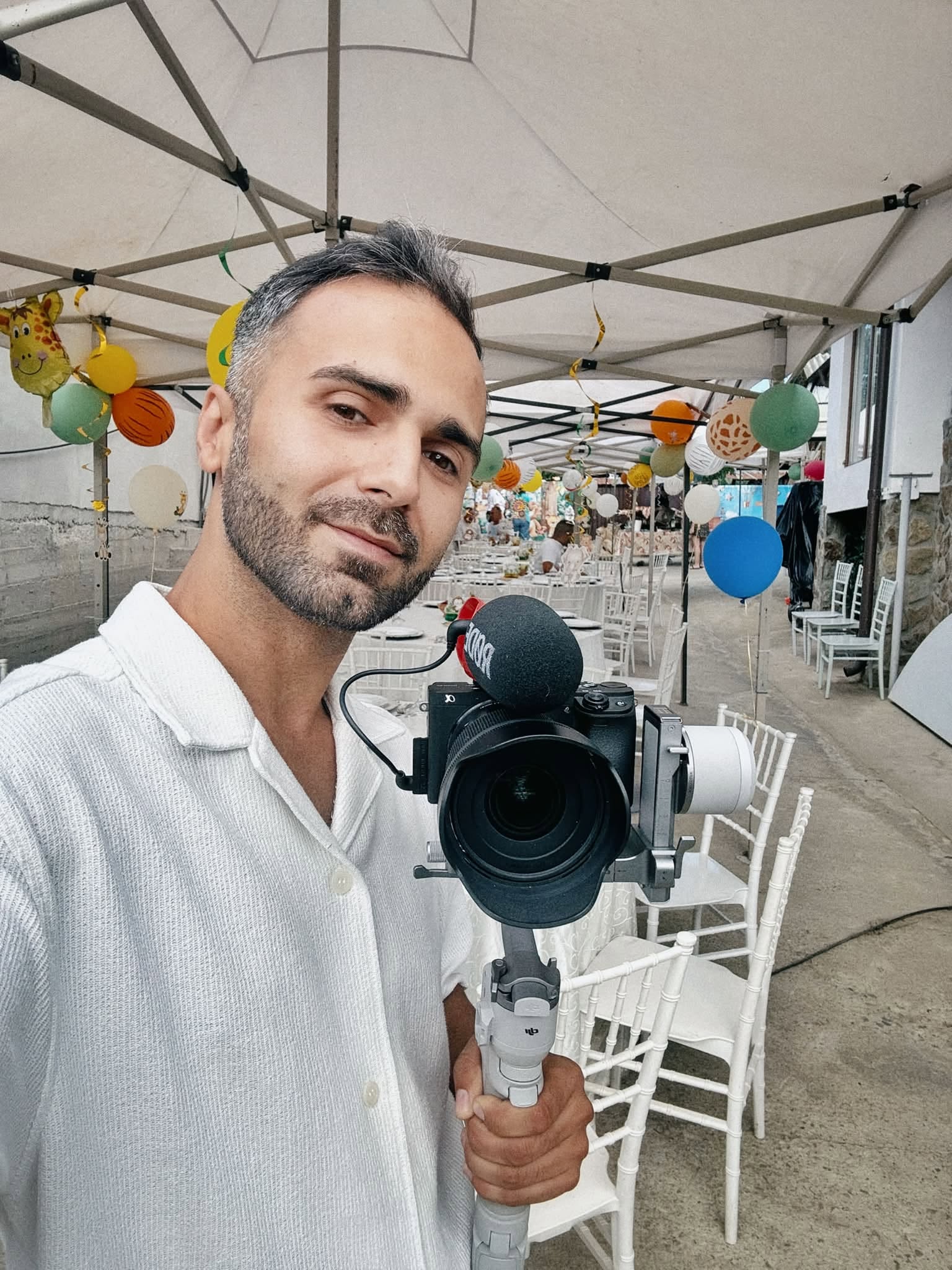 Fotograful George&nbsp;Spineanu la un eveniment, cu camera &icirc;n m&acirc;nă, &icirc;ntr-un cort alb cu baloane colorate, &icirc;n timp ce și el era &icirc;mbrăcat &icirc;n alb