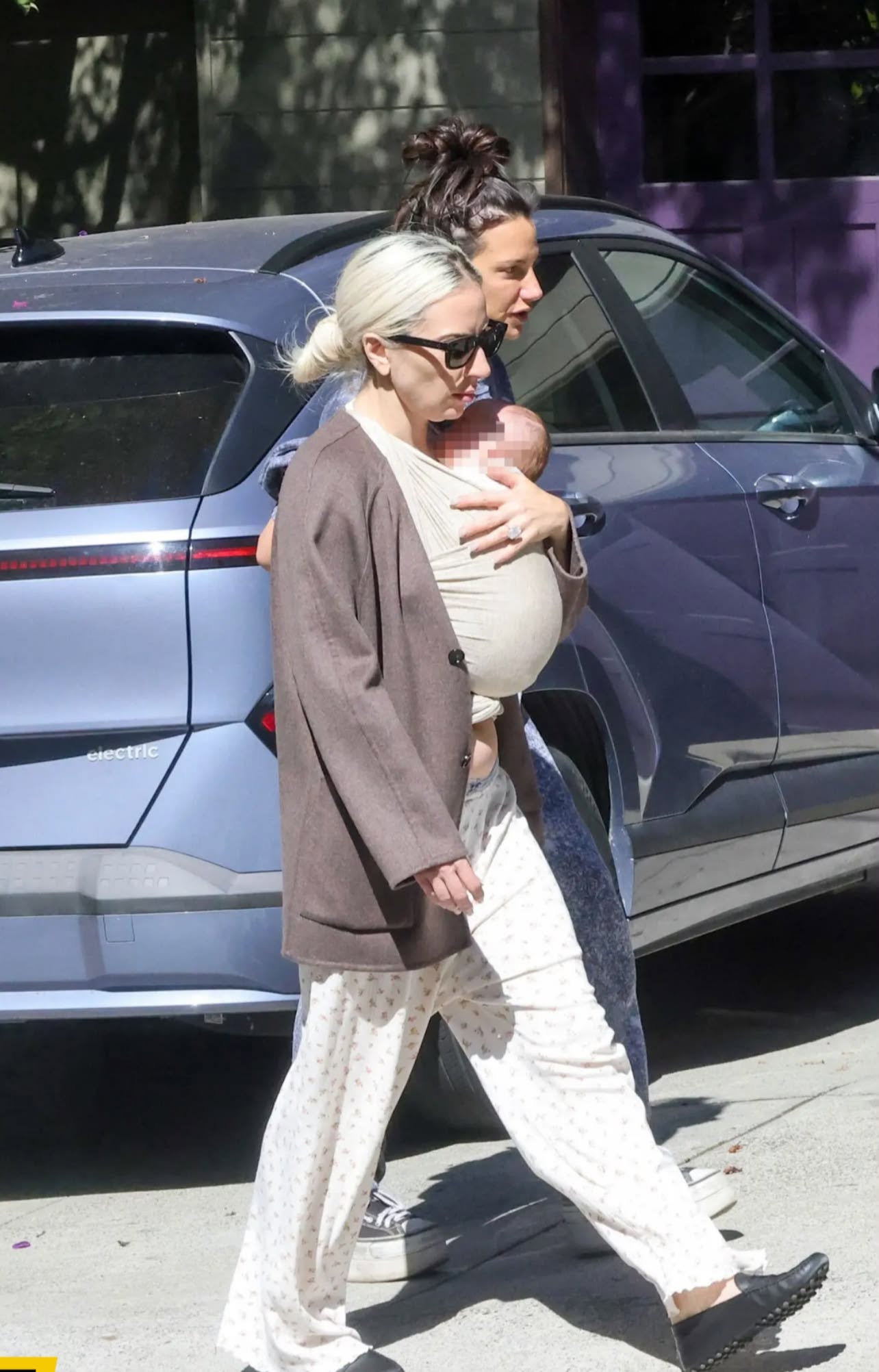 Lady Gaga pe stradă, &icirc;mbrăcată &icirc;n haine lejere, cu părul prin și ochelari de soare la ochi, țin&acirc;ndu-și bebelușul &icirc;n brațe