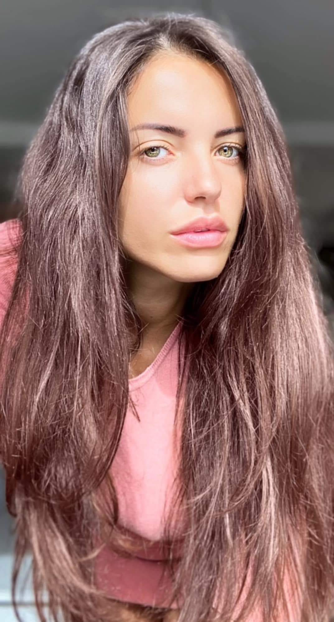 Mădălina Apostol îmbrăcată în roz, făcându-și un selfie cu părul desfăcut, stând aplecată spre camera telefonului