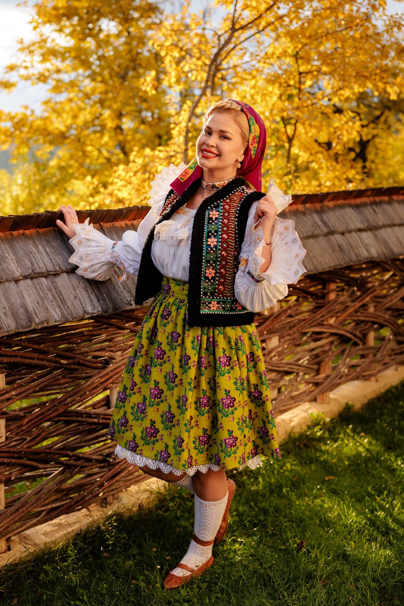 Oana Tomoiagă în costum popular, zâmbitoare, sprijinindu-se de un gard de lemn