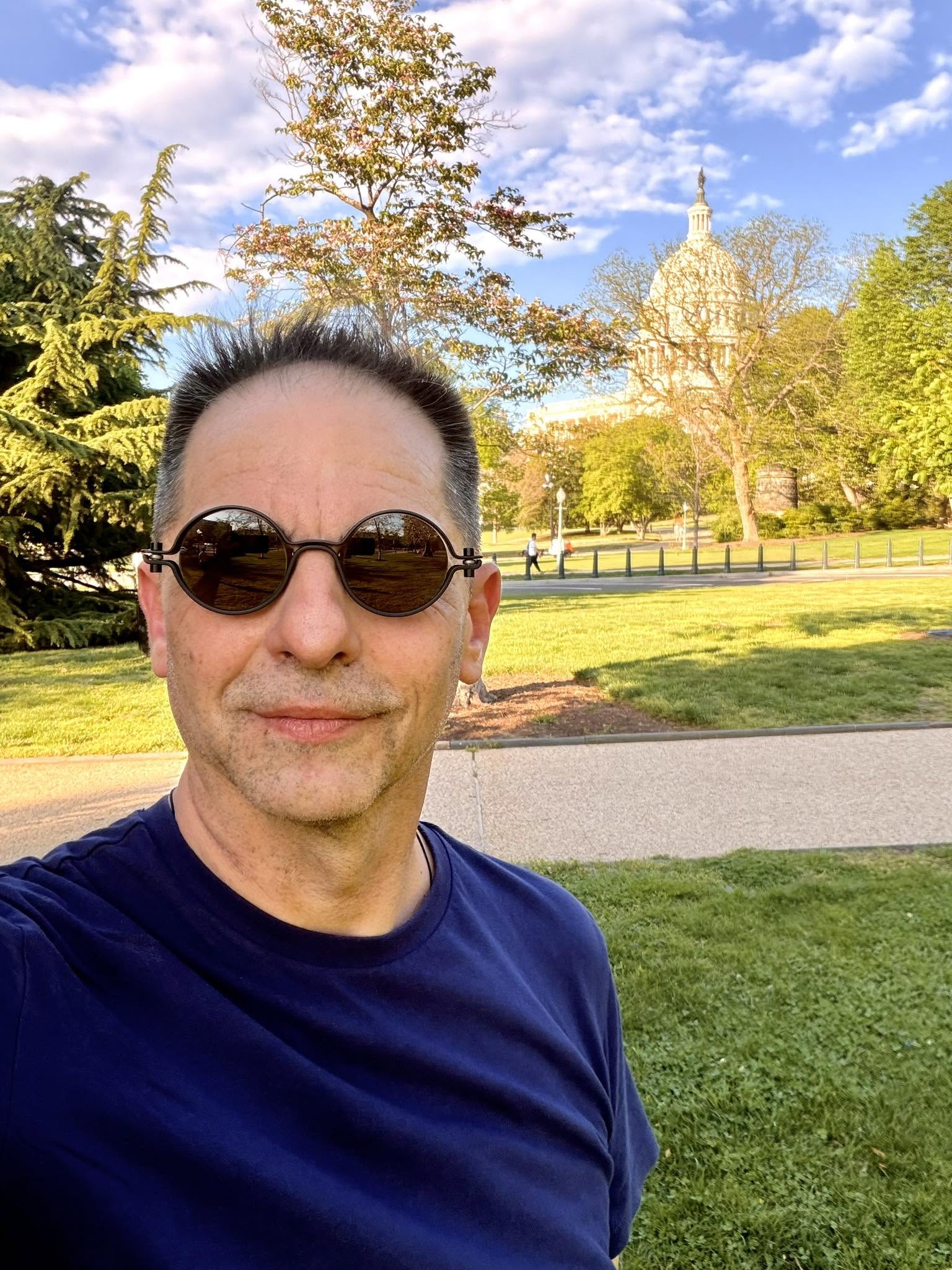 Dan Negru &icirc;ntr-un parc, st&acirc;nd la umbră și făc&acirc;ndu-și un selfie cu ochelarii de soare la ochi