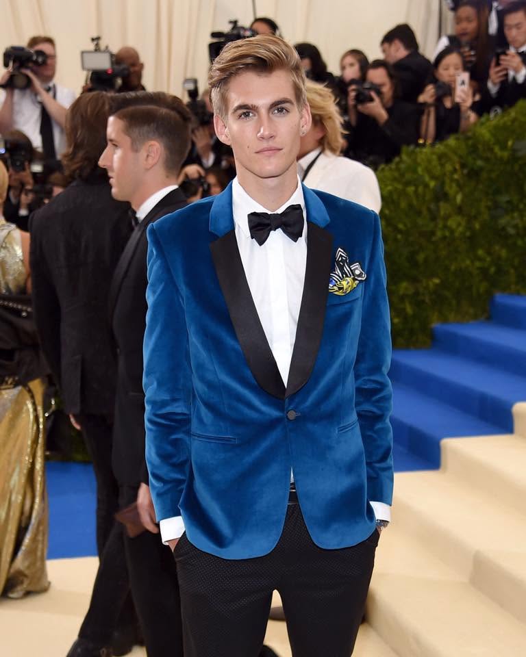 Presley Gerber &icirc;ntr-un costum elegant, format din pantaloni negri, cămașă albă și sacou albastru roial, cu rever negru, st&acirc;nd cu m&acirc;inile &icirc;n buzunar pe niște trepte la MetGala &icirc;n 2017