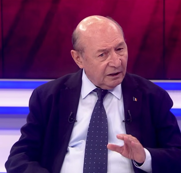 Traian Băsescu &icirc;n platoul Rom&acirc;nia TV, gesticul&acirc;nd &icirc;n timp ce dialoga cu realizatorul emisiunii, &icirc;mbrăcat &icirc;n costum bleumarin, cu cămașă albă și cravată bleumarin cu picățele