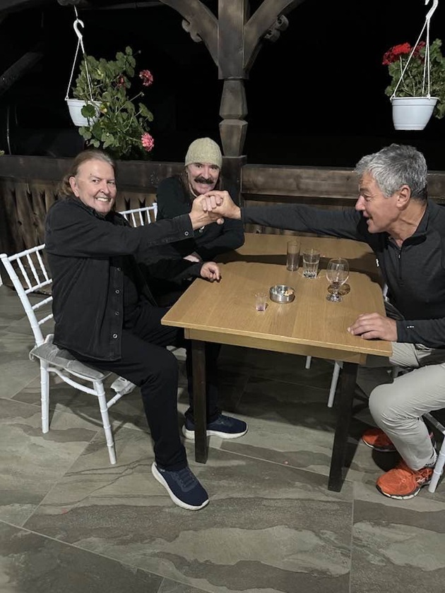 Ducu Bertzi, Vasile Șeicaru și Adrian Păduraru str&acirc;ng&acirc;ndu-și m&acirc;inile deasupra mesei la care stăteau &icirc;mpreună la ceas de seară, &icirc;mbrăcați &icirc;n haine cu m&acirc;necă lungă
