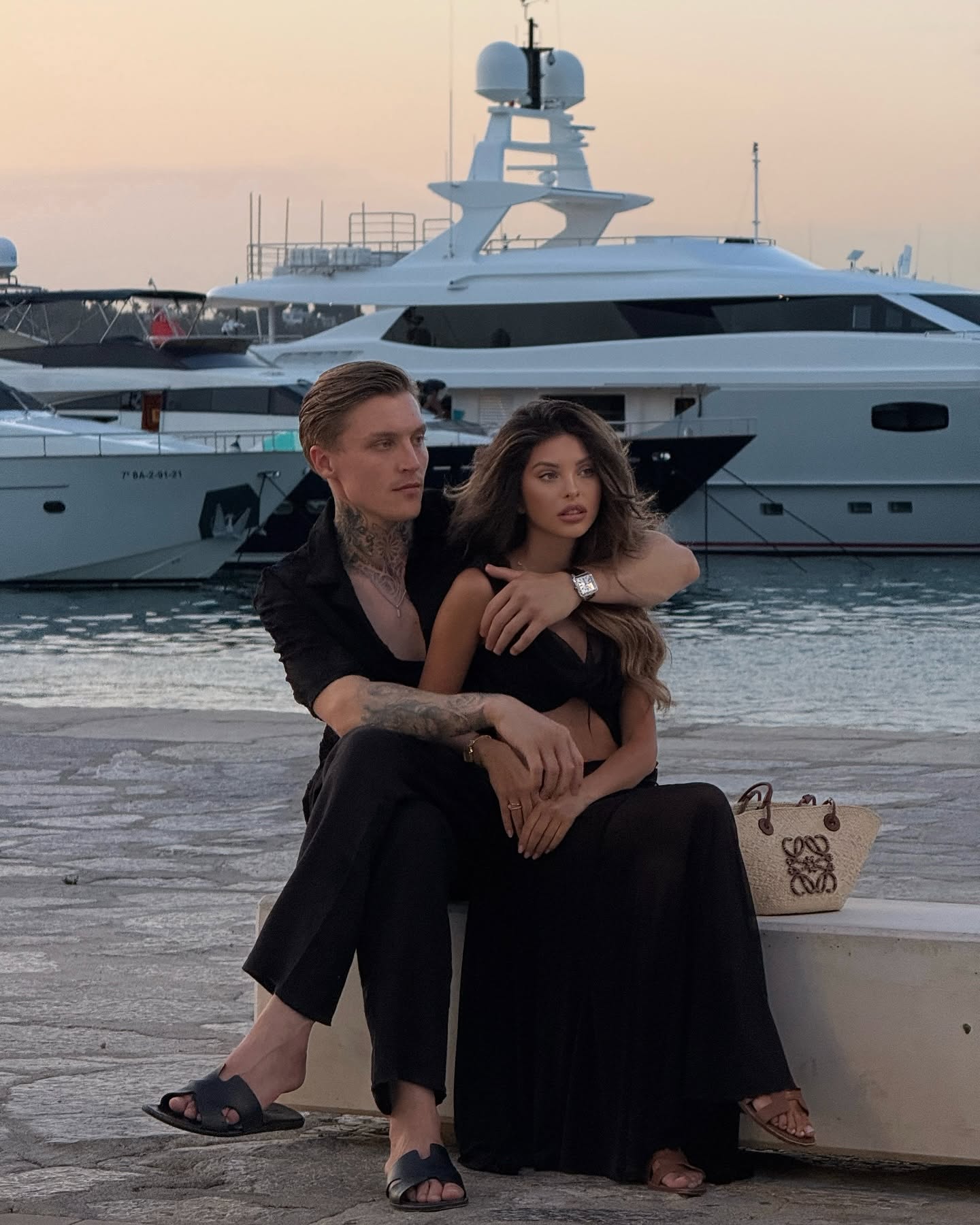 Valerie Lungu &icirc;n brațele lui Alex G&icirc;lcă st&acirc;nd &icirc;ntr-un port, cu mai multe vapoare &icirc;n spate, &icirc;n timp ce erau am&acirc;ndoi &icirc;mbrăcați &icirc;n negru
