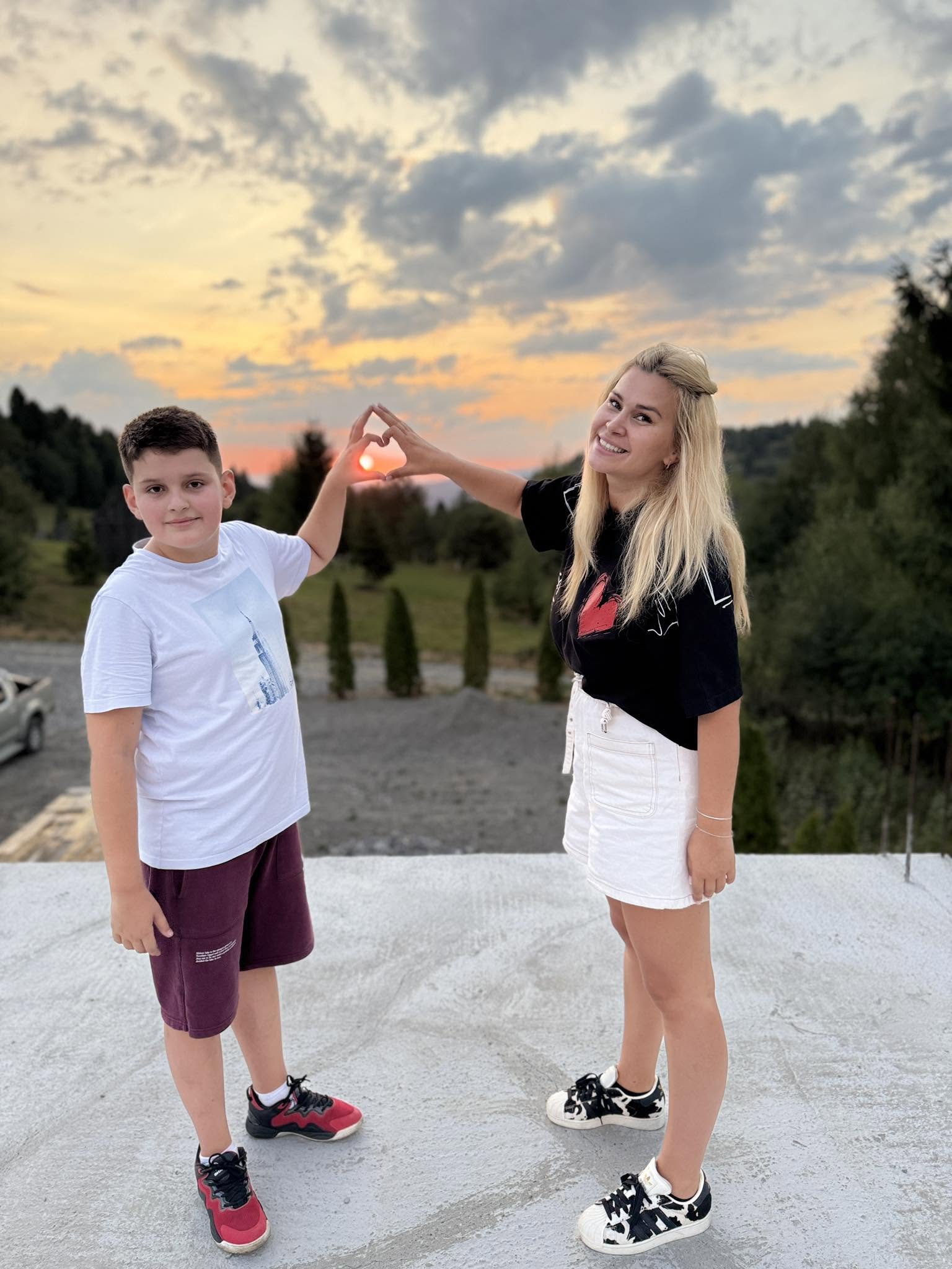 Oana Tomoiagă alături de fiul ei Vlad, &icirc;ntr-un peisaj montan, admir&acirc;nd apusul și &icirc;ncadr&acirc;nd soarele &icirc;ntr-o formă de inimă făcută de m&acirc;inile lor