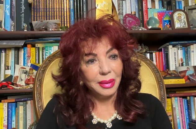 Carmen Harra &icirc;n lacrimi, &icirc;ntr-un tricou negru, cu mărgele la g&acirc;t, &icirc;n fața bibliotecii sale din casa ei din America