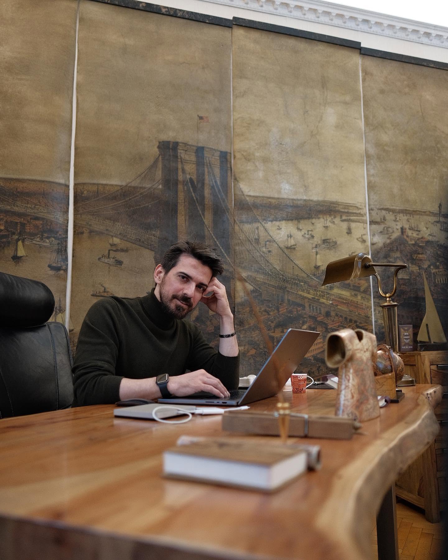 Tuncay Ozturk st&acirc;nd la un birou, cu laptopul &icirc;n față, sprijinindu-și capul de propria m&acirc;nă