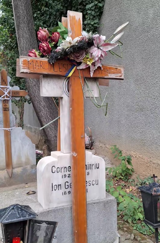 Crucea de lemn distrusă de timp de la morm&acirc;ntul lui&nbsp;Costin Mărculescu, pe care sunt așezate niște flori artificiale și o panglică cu tricolorul