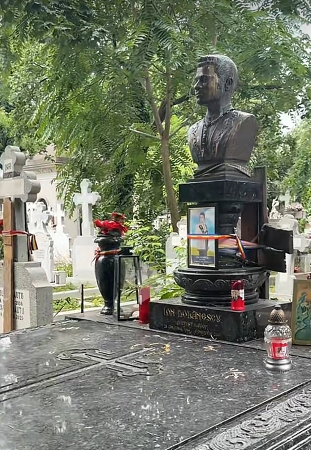 Morm&acirc;ntul lui Ion Dolănescu, acoperit de candele, av&acirc;nd pe piatra funerară o panglică tricoloră și o poză cu el