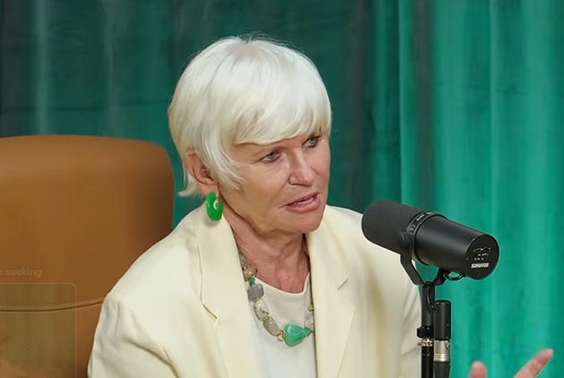 Monica Tatoiu &icirc;n tricou alb și sacou crem, purt&acirc;nd mărgele de mari dimensiuni, &icirc;n cadrul unui podcast, &icirc;n timp ce vorbea la microfon
