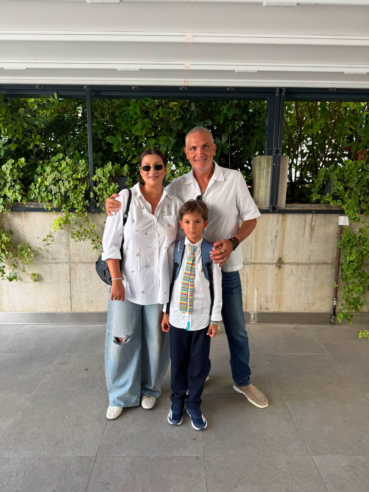 Damian Drăghici și Cristina Stroe alături de fiul lor, Andrei, &icirc;mbrăcat &icirc;n cămașă albă cu cravată colorată și jeanși, purt&acirc;nd un ghiozdan &icirc;n spate