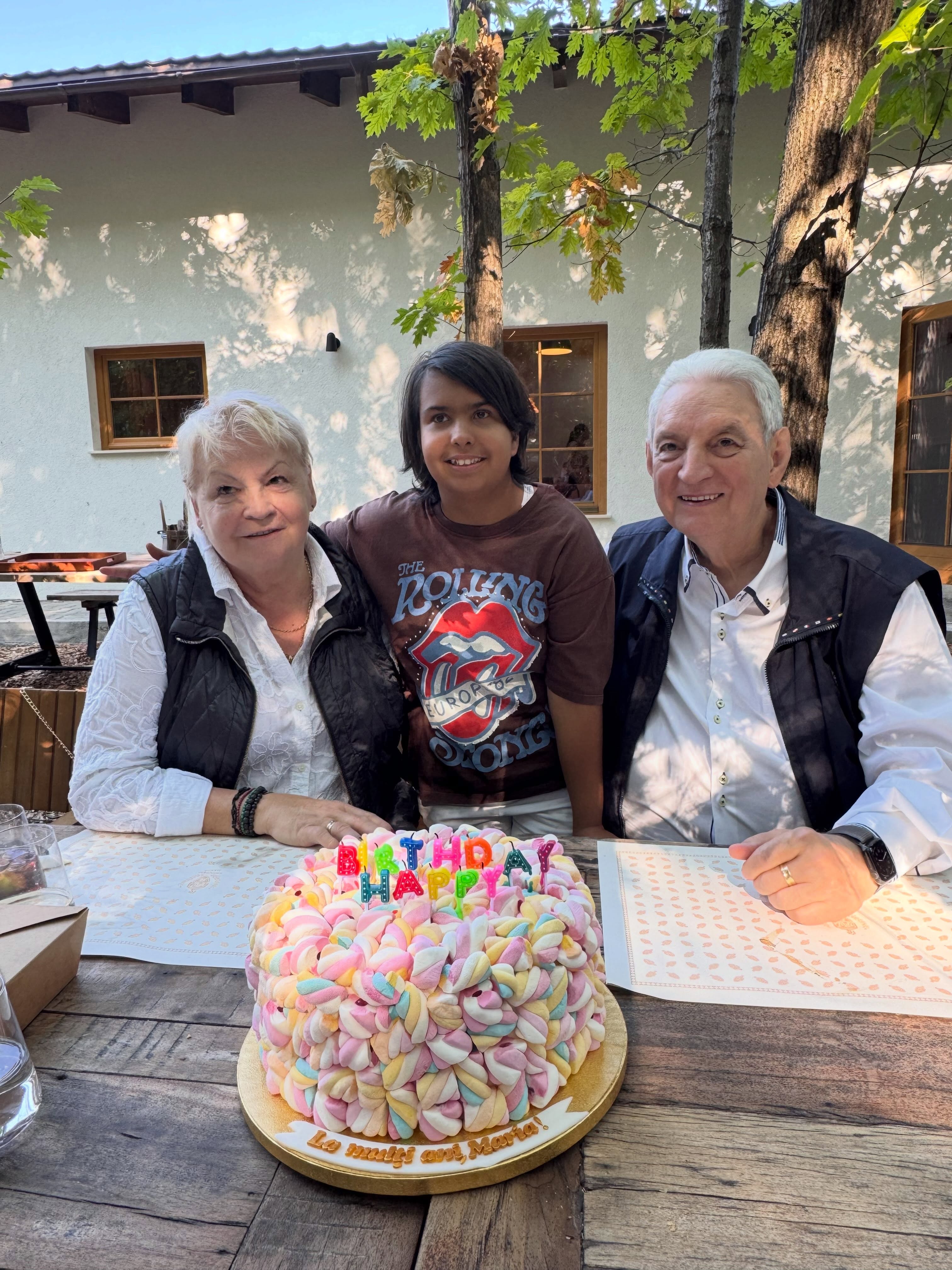 Maria alături de bunicii ei, părinții Dacianei S&acirc;rbu, st&acirc;nd toți la aceeași masă, cu tortul aniversar &icirc;n față