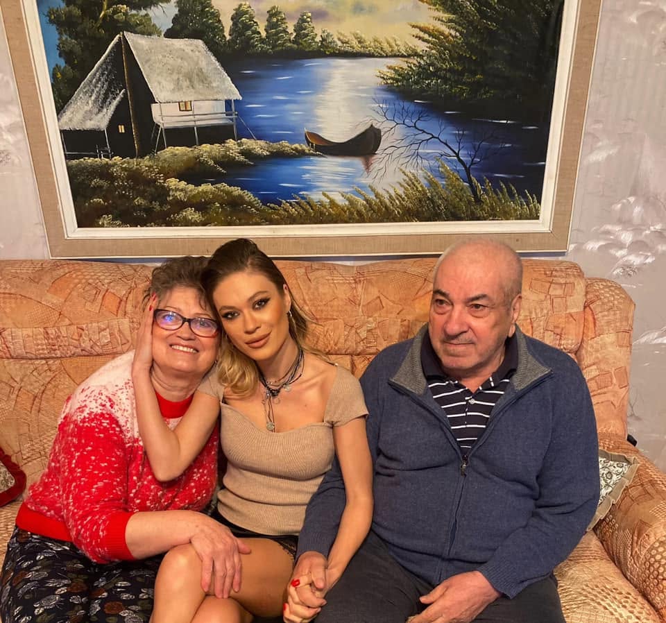 Emma Ștefan st&acirc;nd pe canapea alături de părinții ei și &icirc;mbrățiș&acirc;nd-o pe mama ei, &icirc;n timp ce &icirc;l ținea de m&acirc;nă pe tată