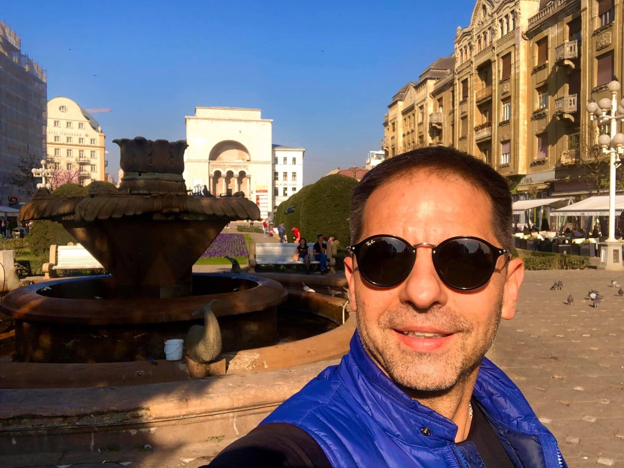 Dan Negru cu ochelari de soare pe străzile din Timișoara, făcându-și un selfie lângă Fântâna cu pești, unul dintre simbolurile orașului