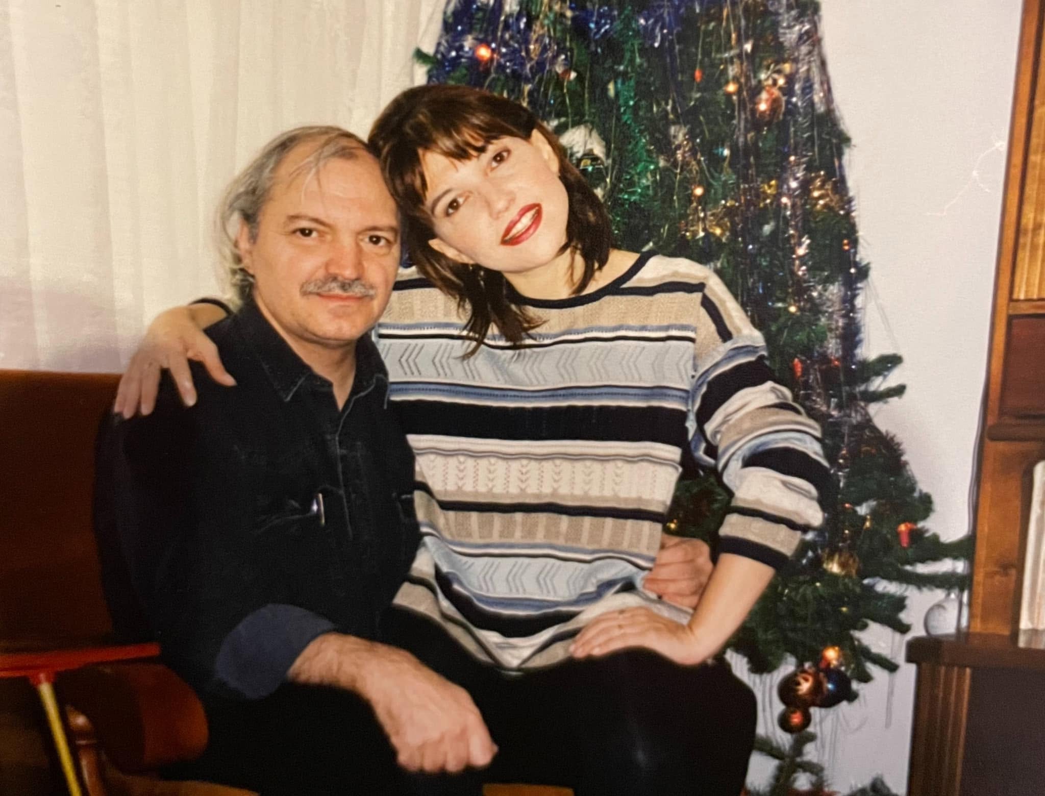 Marina Almășan st&acirc;nd pe picioarele lui Victor Socaciu și cuprinz&acirc;ndu-l &icirc;n brațe, &icirc;n timp ce acesta era așezat pe o canapea, l&acirc;ngă bradul de Crăciun