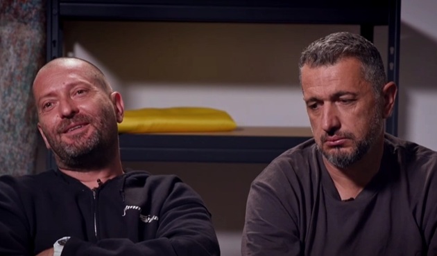 Cheloo și Mihai Ban după ce au aflat că au fost eliminați din competiție, st&acirc;nd unul l&acirc;ngă altul, &icirc;mbrăcați &icirc;n haine &icirc;nchise la culoare, &icirc;n timp ce Cheloo z&acirc;mbea, iar Mihai Ban era g&acirc;nditor