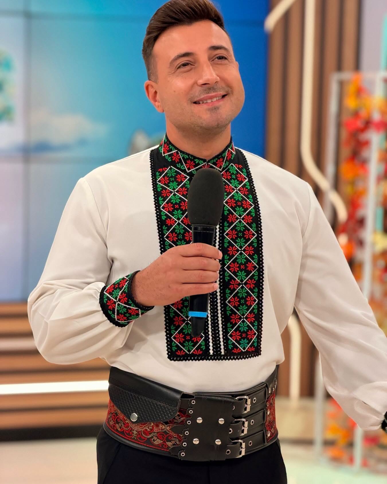 Valentin Sanfira z&acirc;mbitor, cu microfonul &icirc;n m&acirc;nă, &icirc;n costum popular, &icirc;n platoul unei emisiuni.