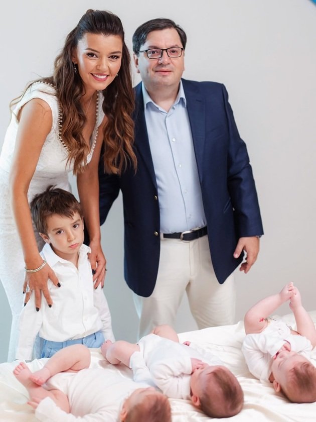 Mihaela și&nbsp;Nicolae Bănicioiu alături de cei patru copii ai lor, &icirc;mbrăcați elegant &icirc;nainte de botezul tripleților, care stateau pe pat, &icirc;n timp ce restul familiei era l&acirc;ngă ei