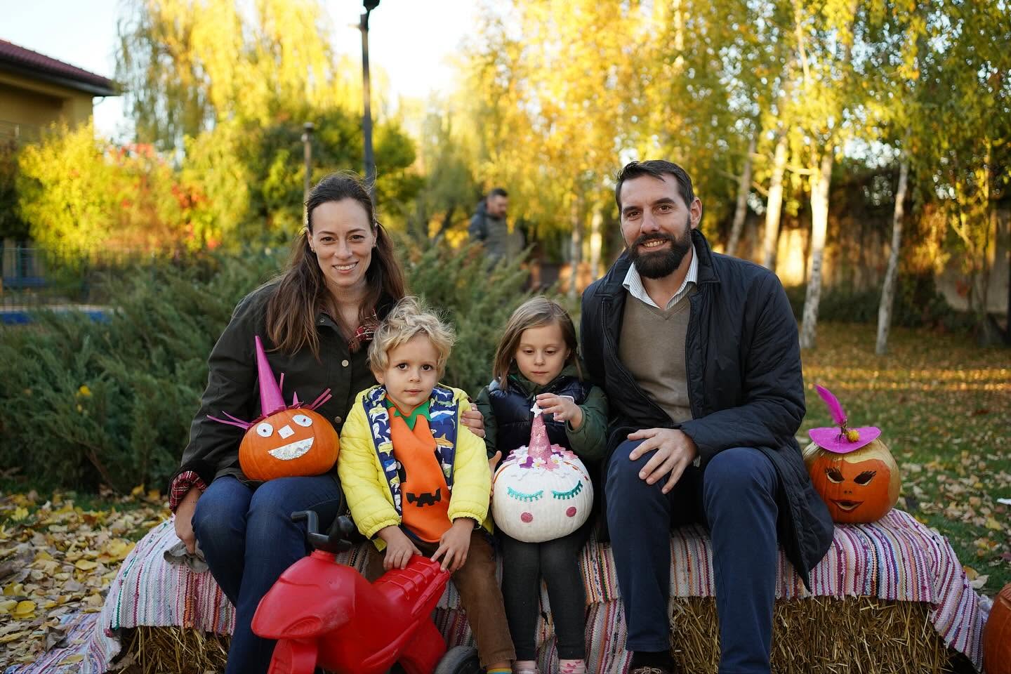 Principe Nicolae și Alina Maria a Rom&acirc;niei alături de copiii lor, st&acirc;nd pe niște baloți de paie, &icirc;ntr-un peisaj de toamnă, țin&acirc;n &icirc;n m&acirc;nă dovleci pictați