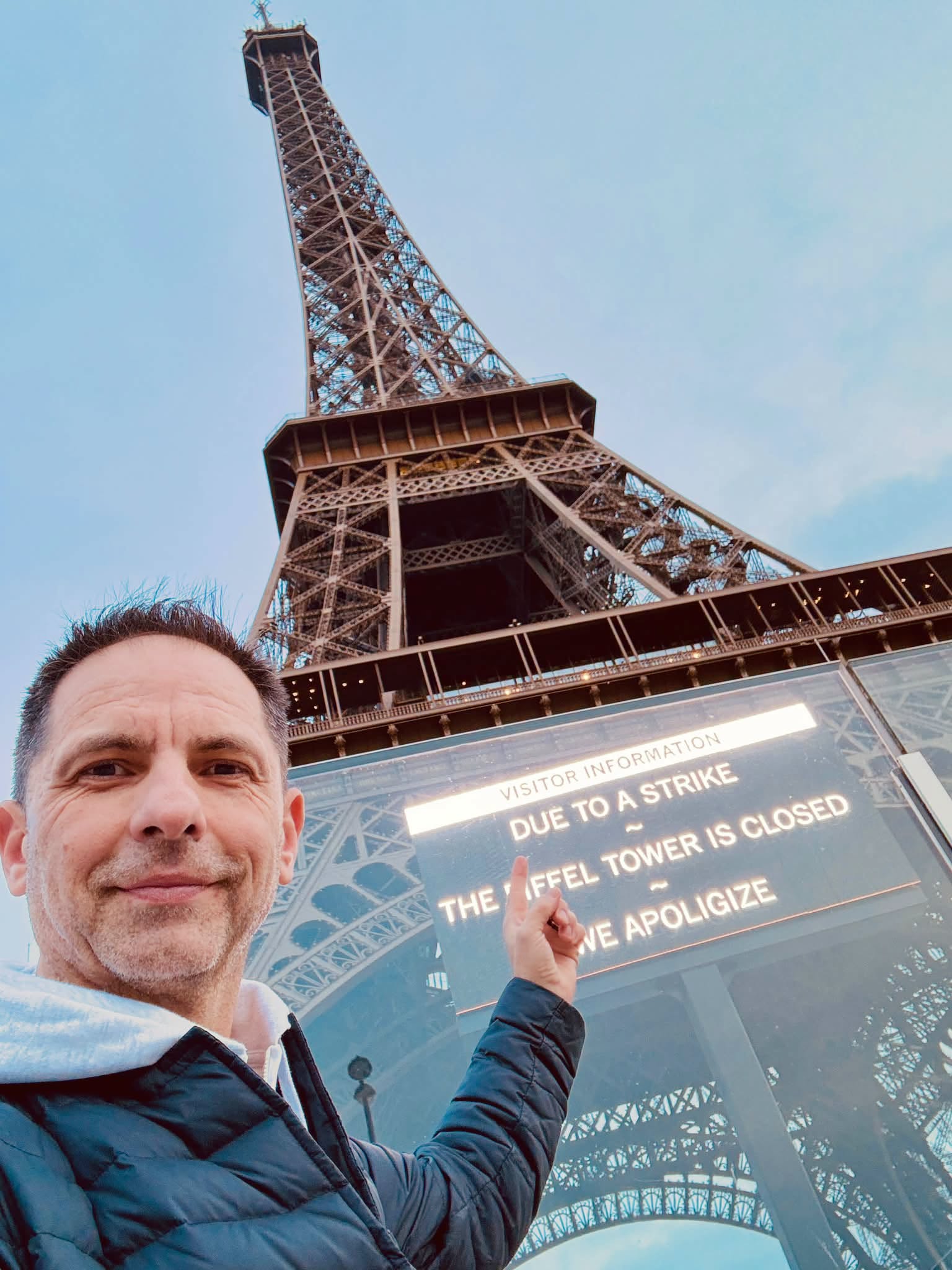 Dan Negru lângă Turnul Eiffel, arătând mesajul scris pe monument, în care administratorii își cer scuze că Turnul este închis și nu îi pot lăsa să urce în el