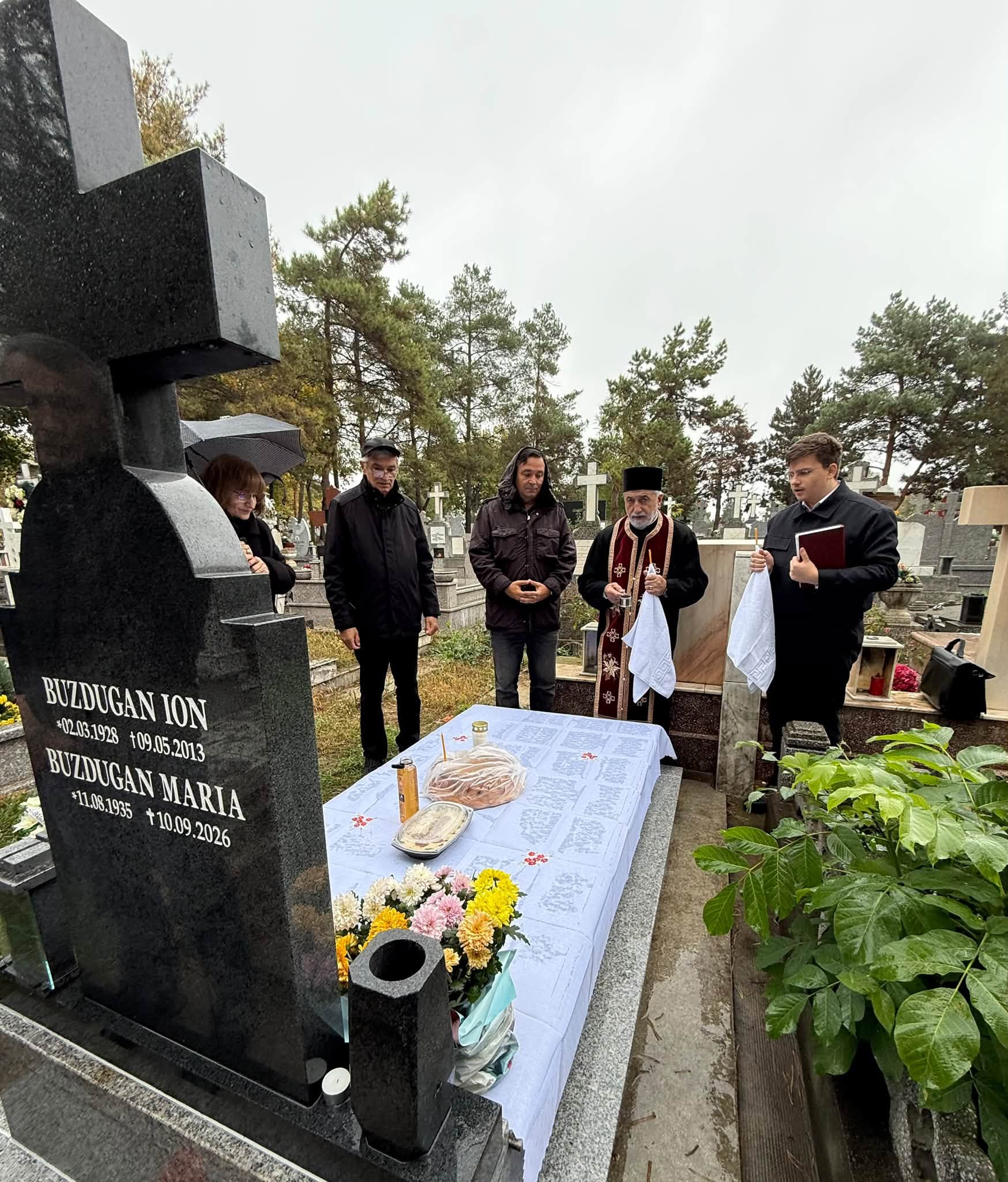 Daniel Buzdugan și fratele său, alături de preot la mormântul părinților, la 40 de zile de la decesul mamei lor, stând în ploaie la slujba de pomenire