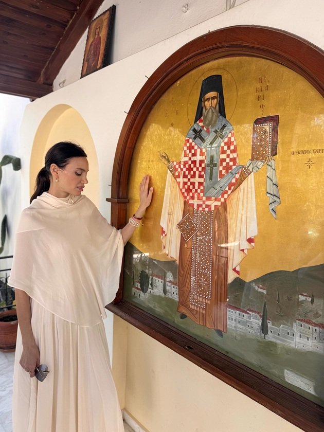 Alina Pușcău rug&acirc;ndu-se &icirc;n fața unei icoane de mari dimensiuni, pusă pe peretele exterior al unui lăcaș e cult