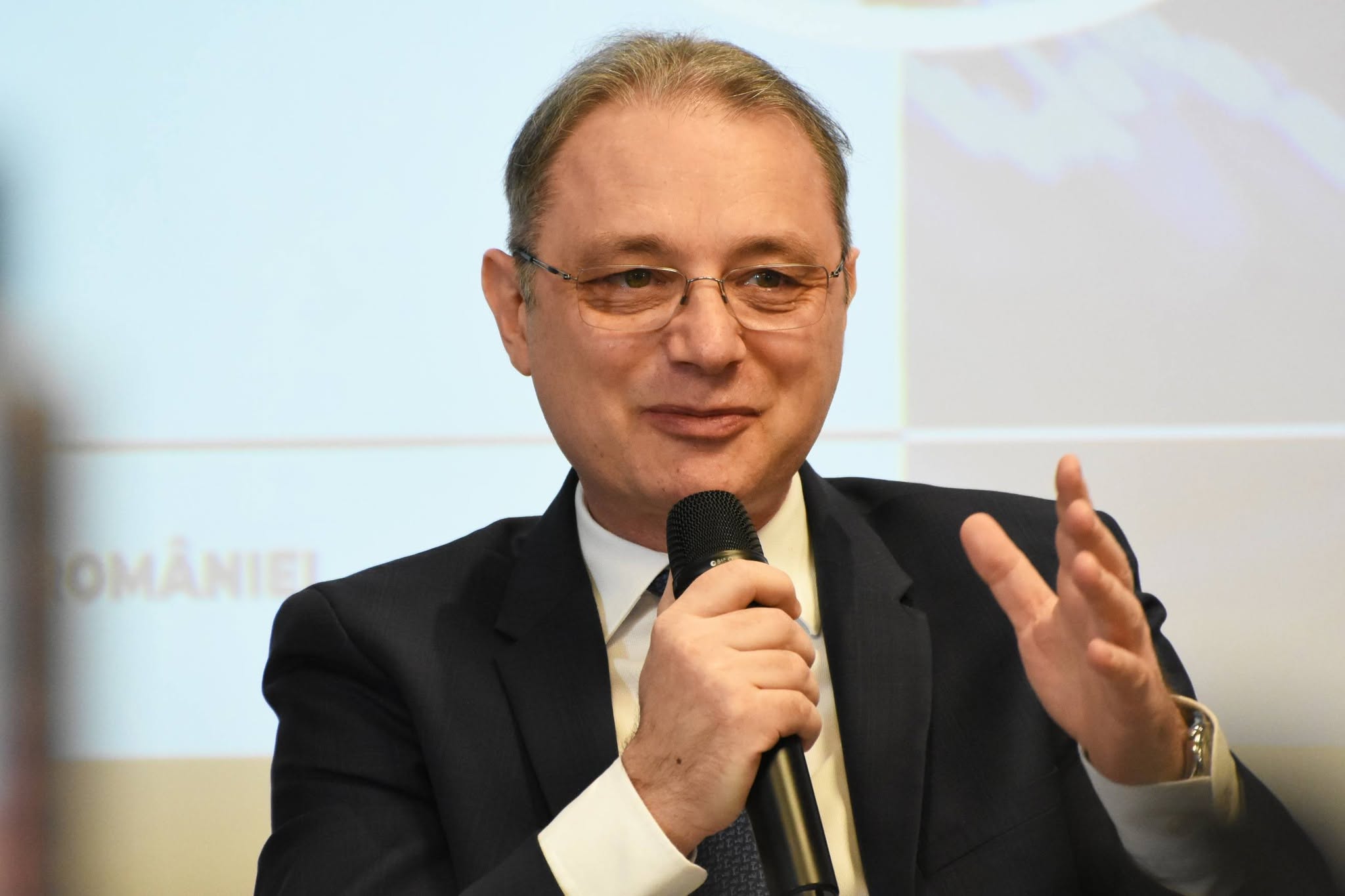 Luca Niculescu, noul premier al Rom&acirc;niei, &icirc;mbrăcat &icirc;n sacou negru, cămașă albă, țin&acirc;nd &icirc;n m&acirc;nă un microfon, &icirc;n timp ce vorbea &icirc;n fața unei audiențe