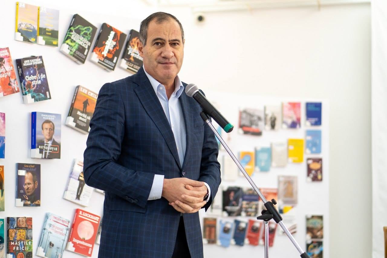 Marian Neacșu vorbind la microfon, l&acirc;ngă un perete plin cu cărți, &icirc;n timp ce purta un saciu bleumarin &icirc;n carouri și o cămașă bleu și &icirc;ți ținea m&acirc;inile &icirc;mpreunate