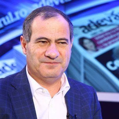 Marian Neacșu z&acirc;mbitor, purt&acirc;nd un sacou bleumarin cu pătrățele și o cămașă albă, av&acirc;nd un microfon de lavalieră atașat la reverul sacoului